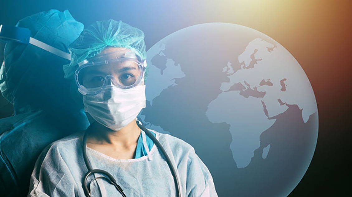 A health professional in PPE standing in front of a globe.