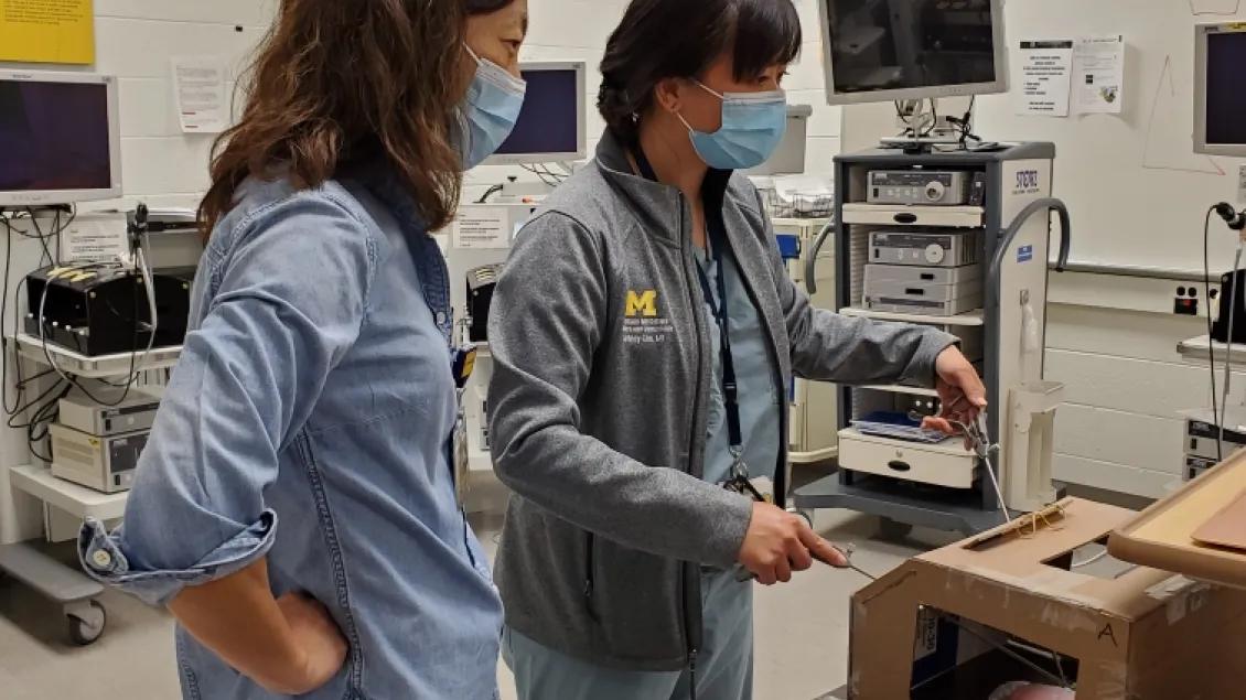 Two people wearing surgical masks looking at a scientific instrument made out of a cardboard box