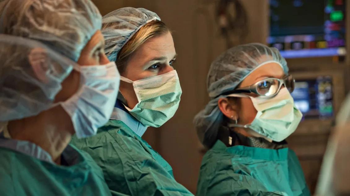 Three women stand in an OR looking at a screen.