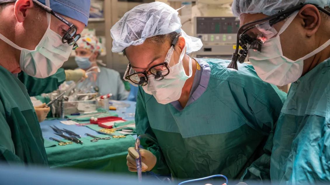 Three people stand over a patient in an operating room. 