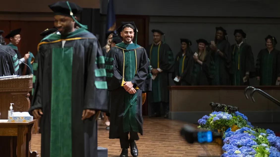 Two graduates cross the stage at MD Commencement while a line waits to proceed