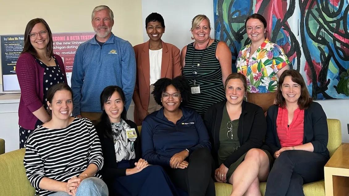 Pediatrics team with 5 people standing and 5 people sitting on yellow couch