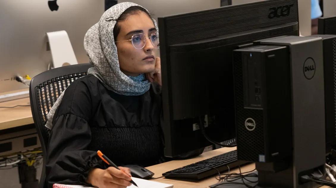 Student takes notes while looking at computer monitor
