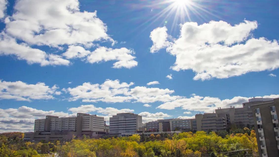 Michigan Medicine campus showing buildings in distance with bright blue sky and white clouds with trees with fall foliage in foreground