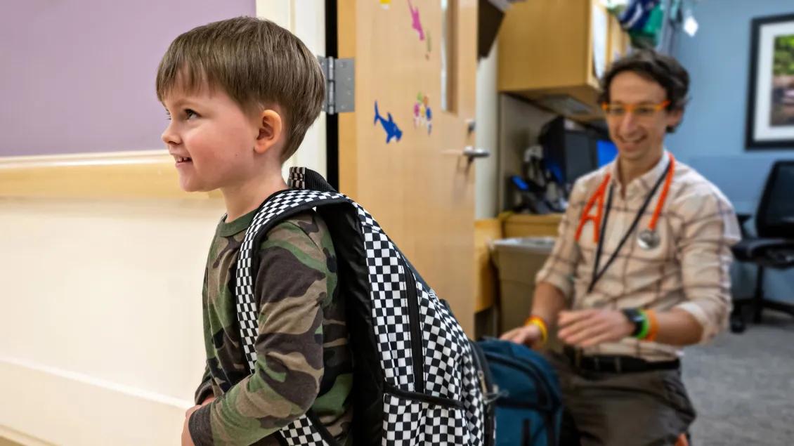 Doctor watches child with backpack walk through hallway