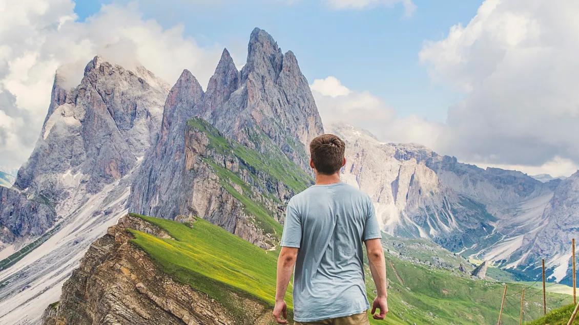 A person standing with their back to us, facing a beautiful mountain scene