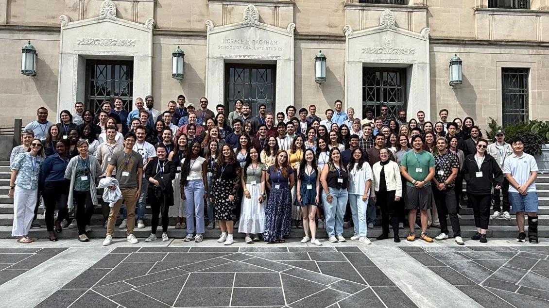 a large group stands in front of a building with stairs