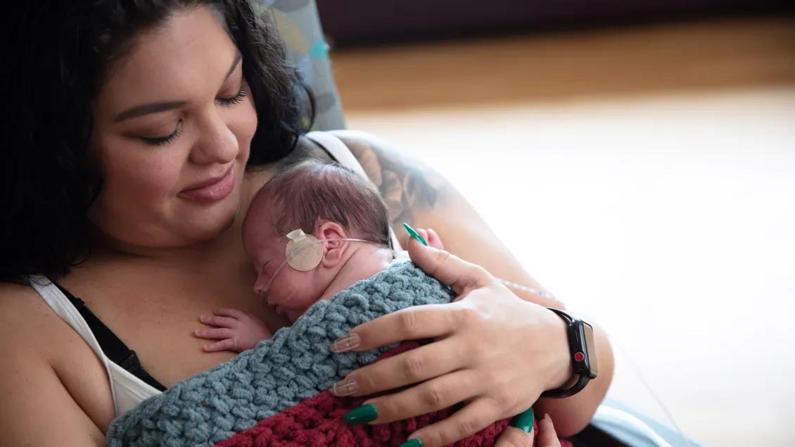 Mother holding her newborn with an oxygen tube, wrapped in a blanket
