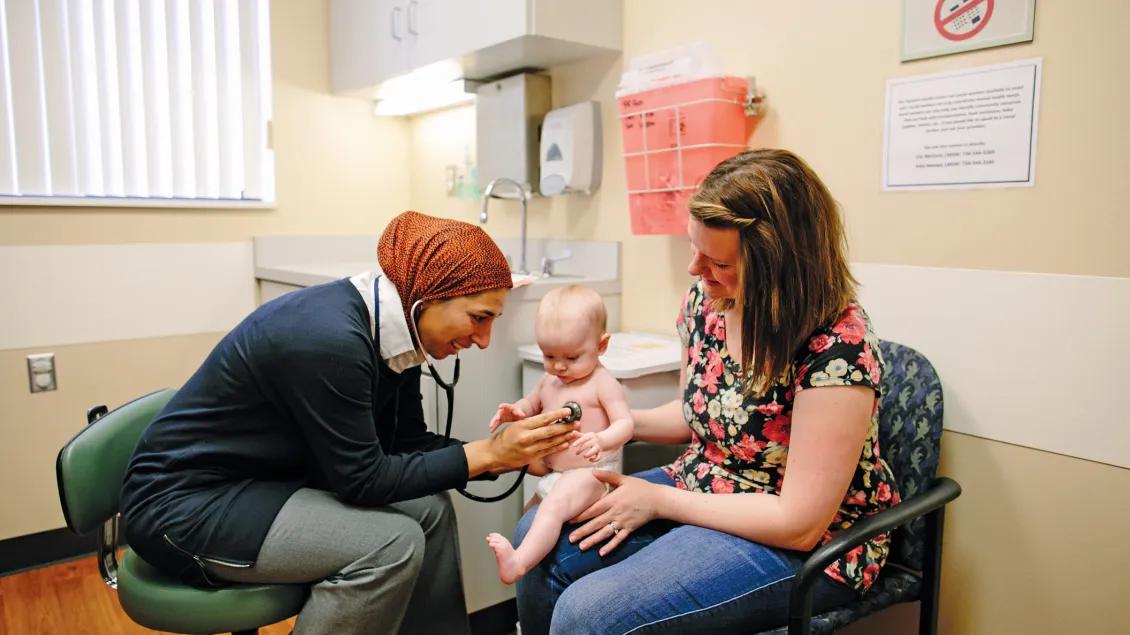 A mother holding a baby in a patient room with a physician