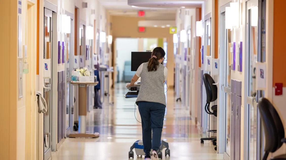 A hospital worker wheeling equipment down a hallway
