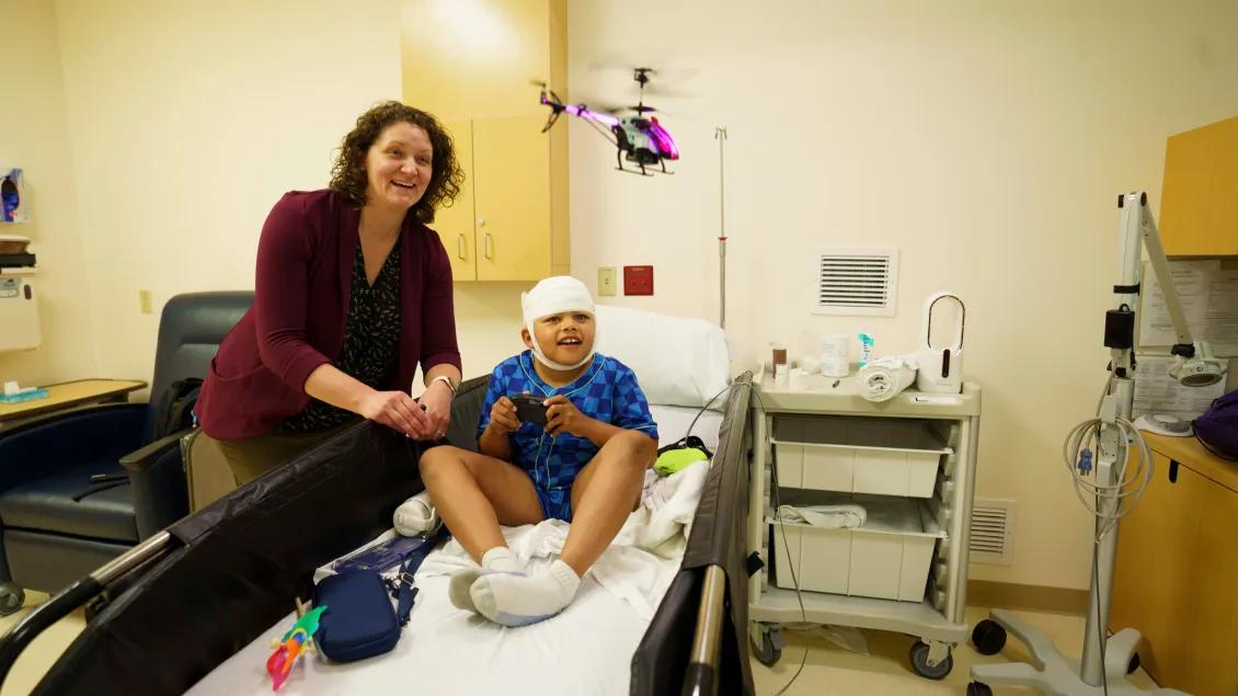 A hospital worker with a pediatric patient sitting in a bed with bandages