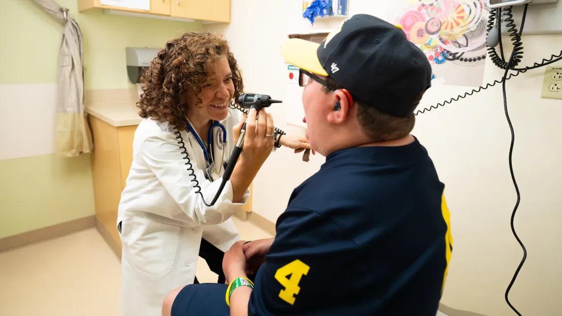 A pediatric doctor examines a young patient’s ear during a checkup, both smiling in a brightly lit clinic room.