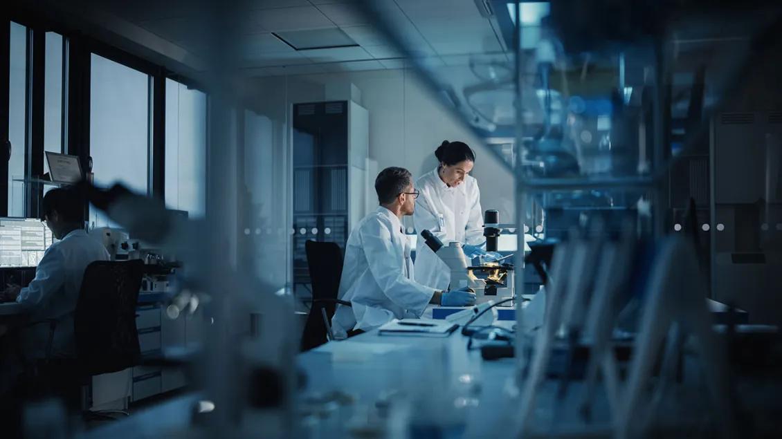 A man and woman work on one side of lab while another man works at a computer