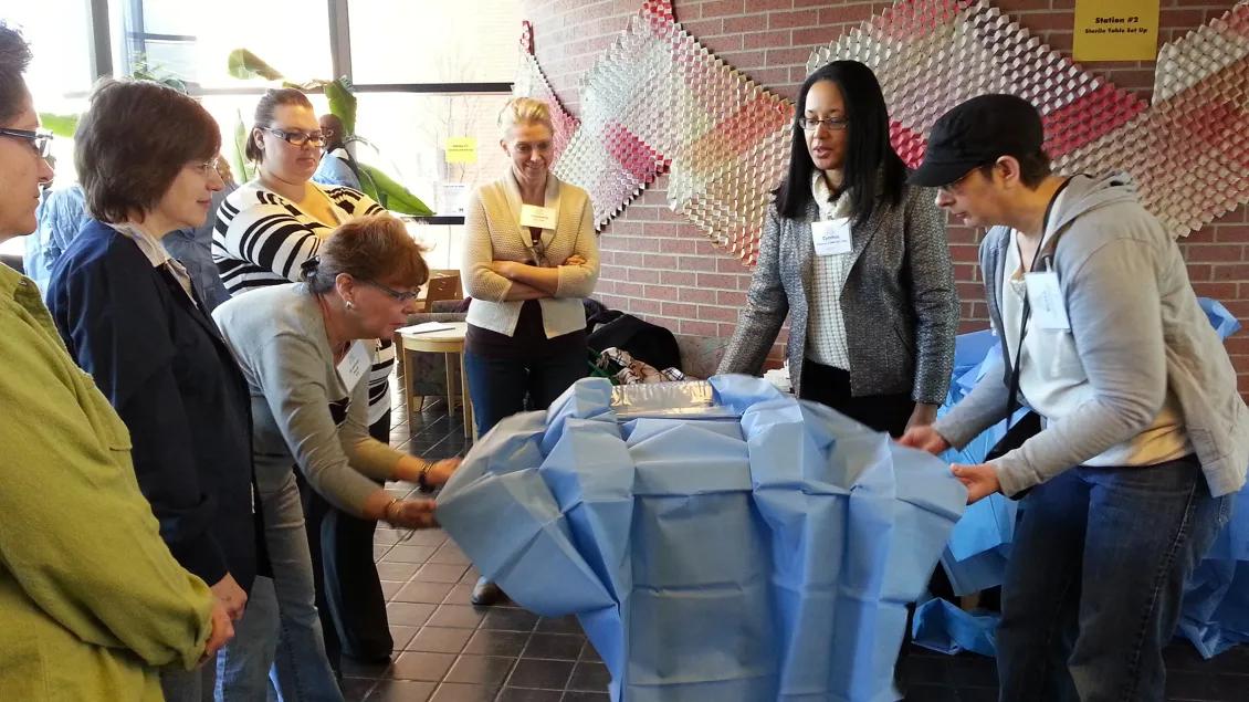 Allied health professionals in a semi-circle around a table covered with a blue cloth and two instructors