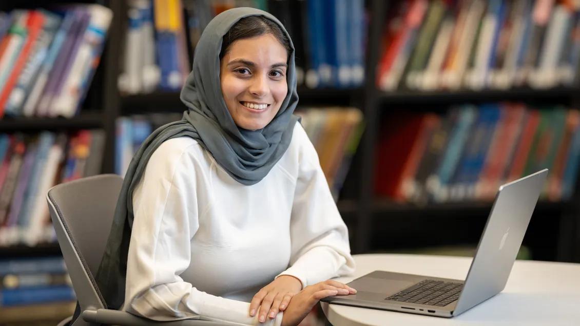 Resident Marium Sohail sitting in front of a laptop with shelves of books behind.