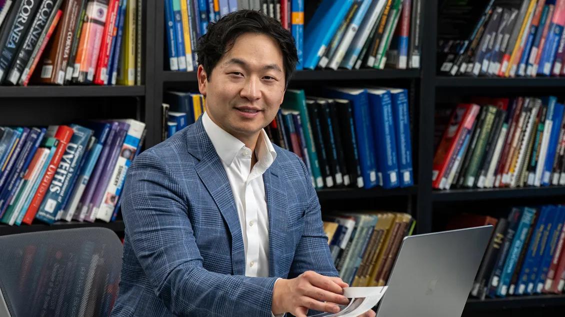 Warren Pan, MD, PhD working at a laptop with shelves of books behind them.