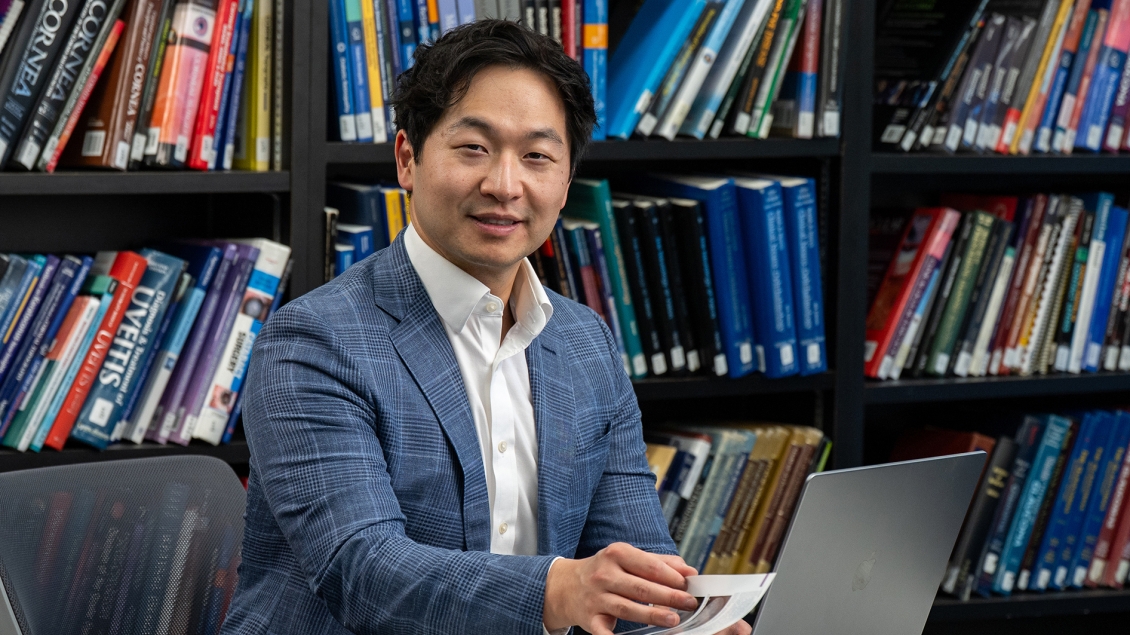 Warren Pan, MD, PhD working at a laptop with shelves of books behind them.