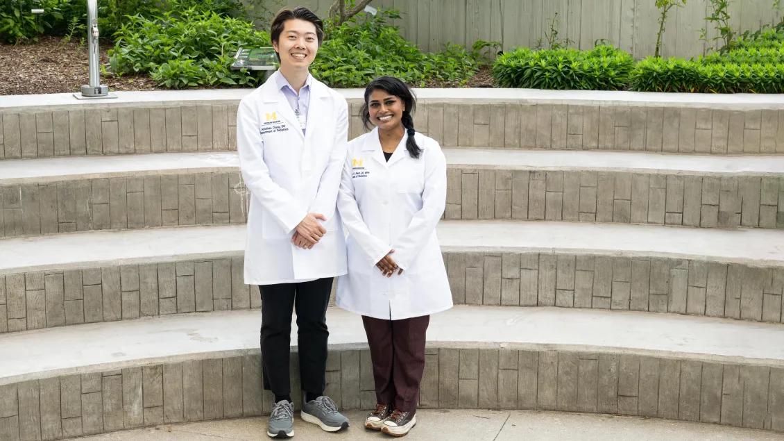 Two smiling Pediatrics Medical Genetics program's residents in white coats standing outside on concrete tiers