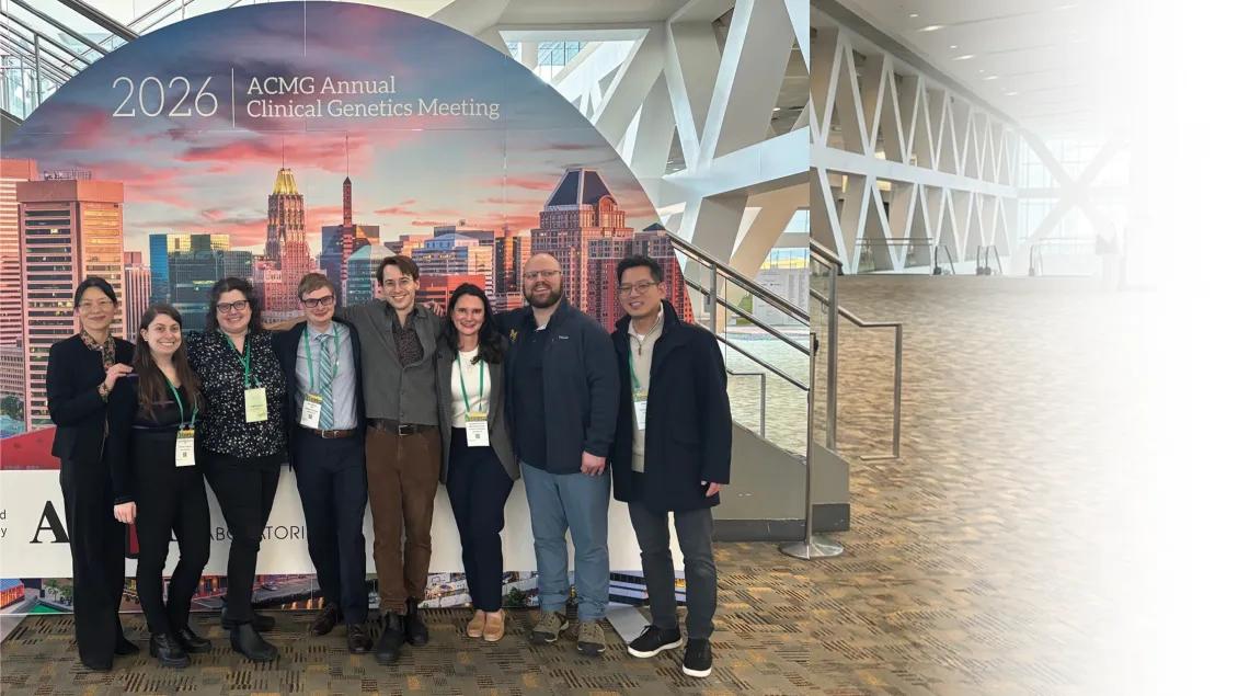 A group of eight medical genetics residents posing together in front of a large backdrop for the 2026 ACMG Annual Clinical Genetics Meeting