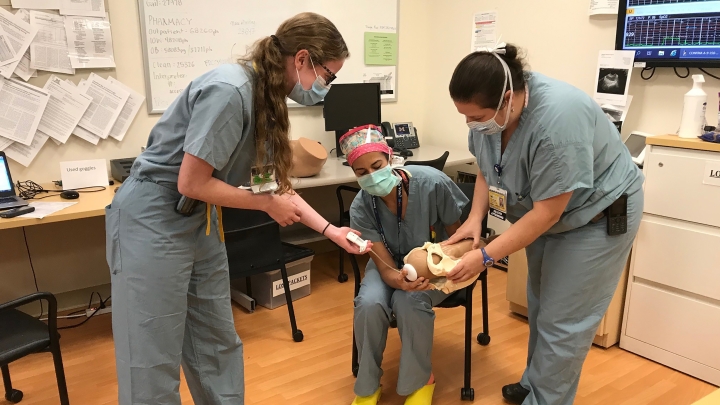nurses gather round to practice holding techniques for a baby 