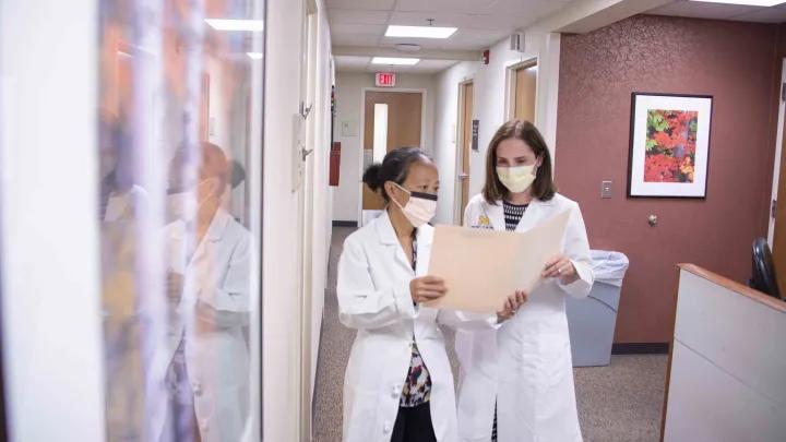 two doctors talk in hallway with file open