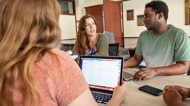 Diverse group of four students seated around a study table talking