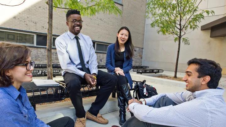 Seated group of diverse students laughing outside campus medical building