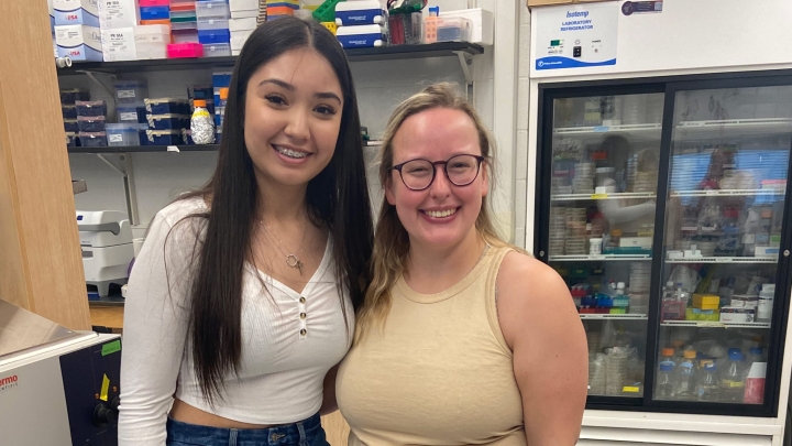 two students smiling and looking at the camera in a lab setting