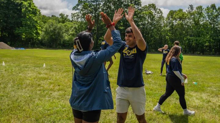 Two college age students give each other a double high five in a field.