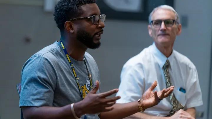 Two diverse men conversing in a group off camera
