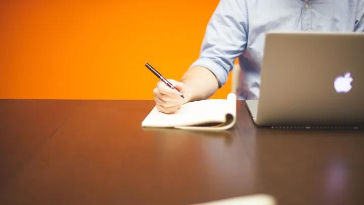 person taking notes in front of a laptop