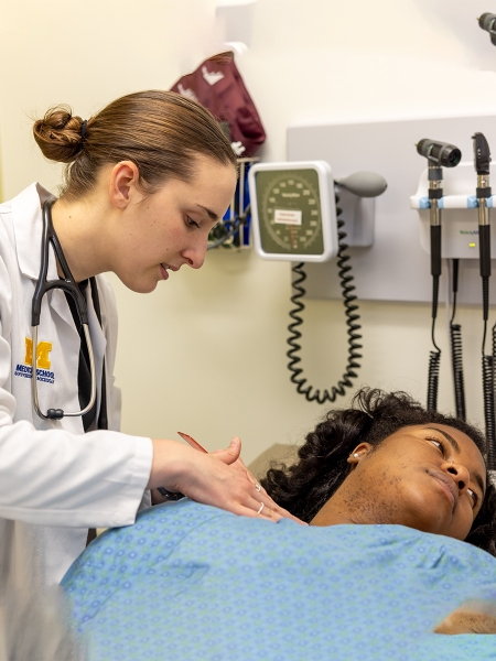Female in white coat with stethoscope examining reclining black female patient
