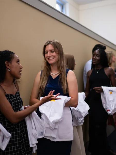 Diverse group of women wearing dresses standing with white medical coats folder over their arms