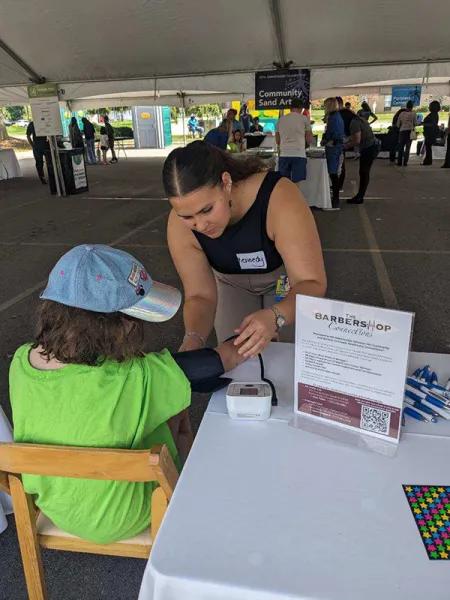 Young woman with name badge helping seated child at table under large tent