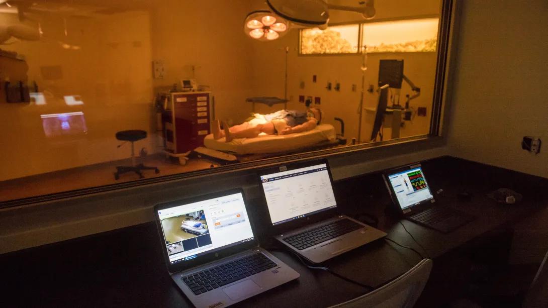 Empty control room with 3 screens and dummy patient viewable in the next room