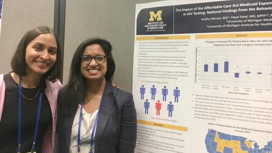 Women in front of michigan medicine board smiling