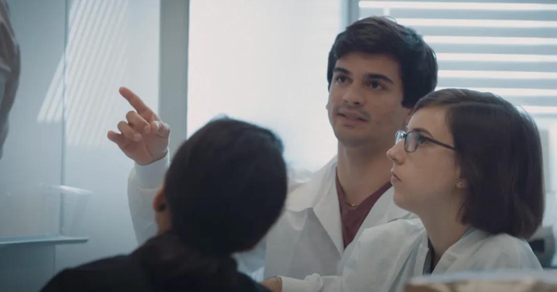three students standing in lab looking at machine 
