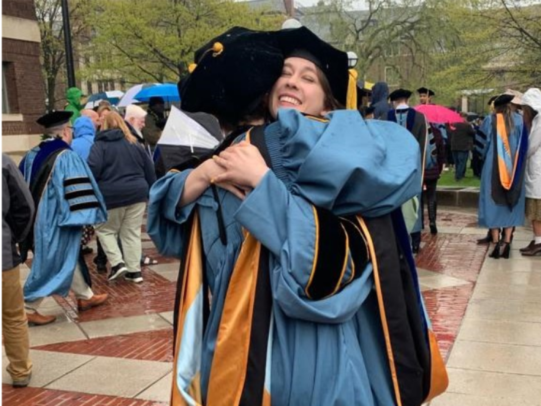 Grad students in gown hugging at graduation 