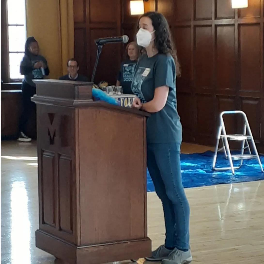 Female lead speaker stands at podium to address the audience 