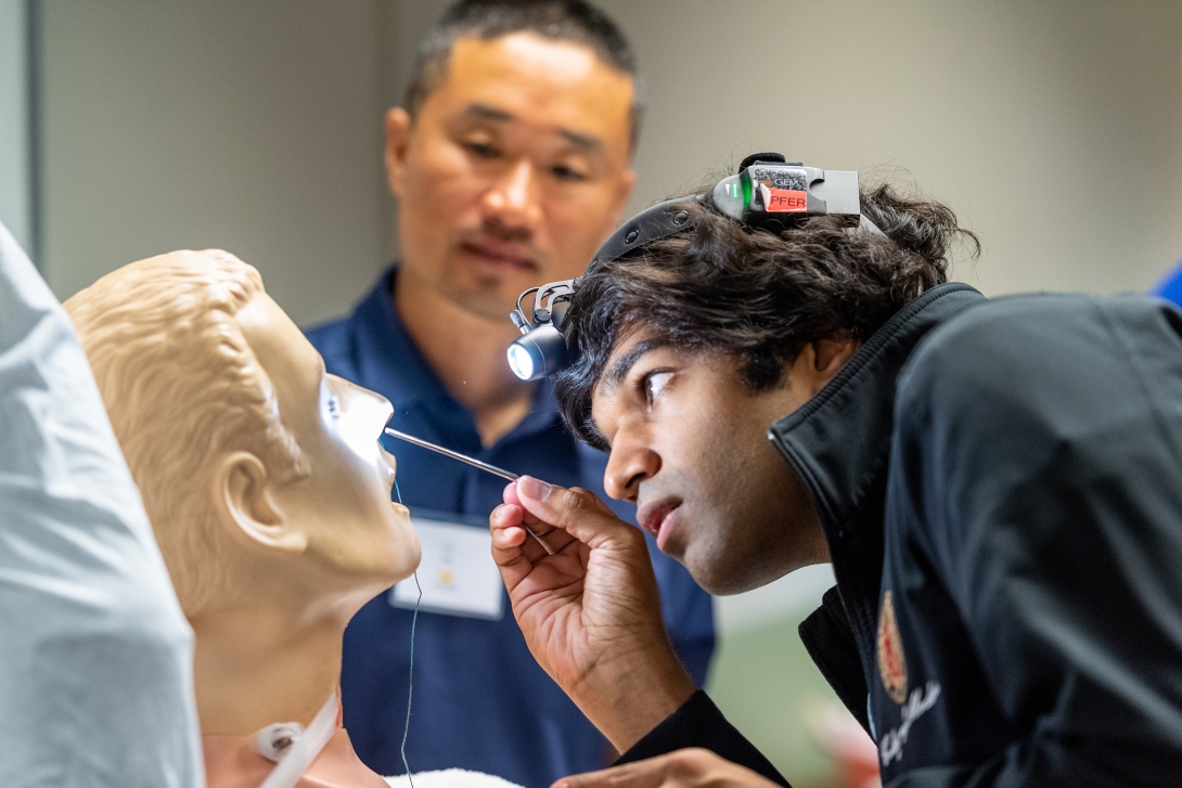 A student practices an exam on a dummy in the simulation lab
