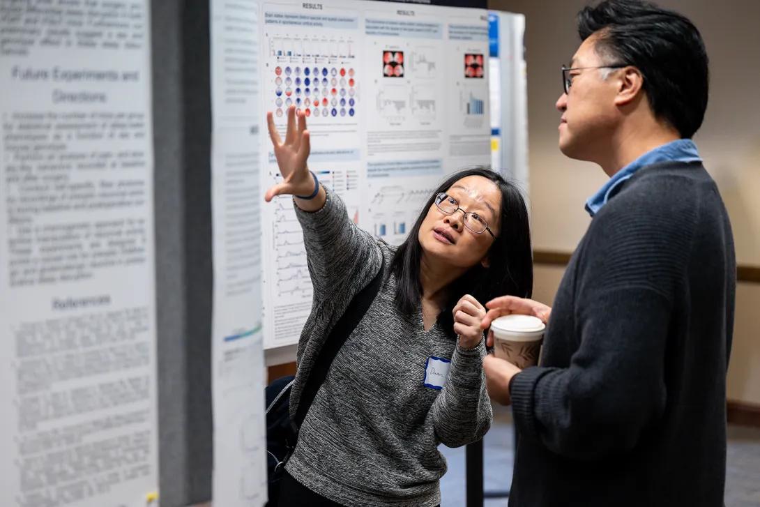 Duan Li gestures at a research poster while speaking with another researcher