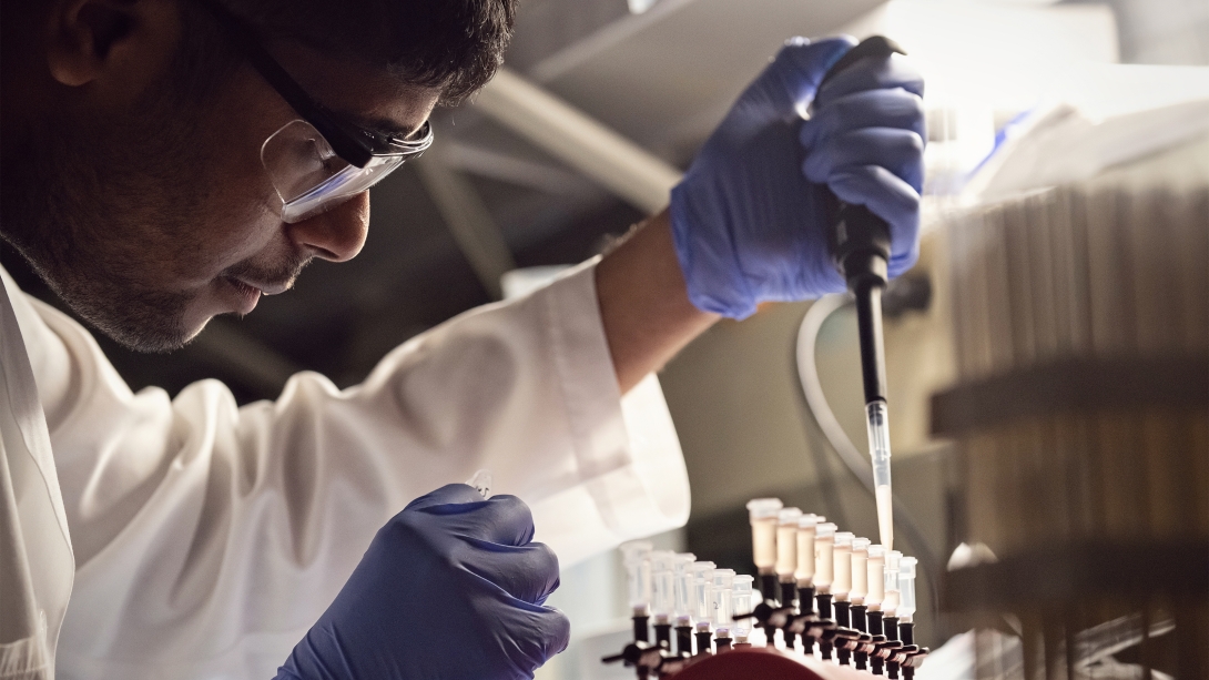 Young brown-skinned male in research lab wearing goggles and blue gloves with test tubes