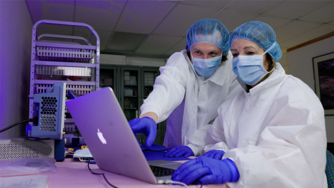 researchers in lab on computer white coats and blue netted hats