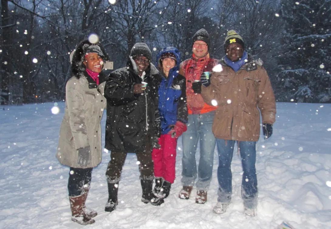 A group of 5 people in winter coats and hats standing out in the snow