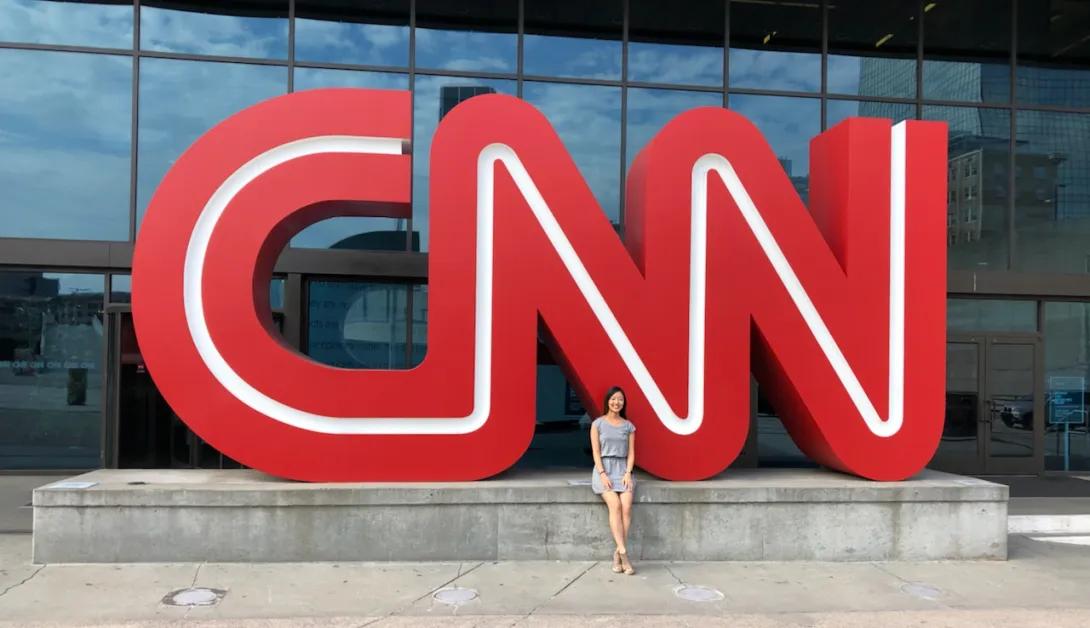 A large statue of the CNN logo in front of a building, with a woman standing in front of the logo