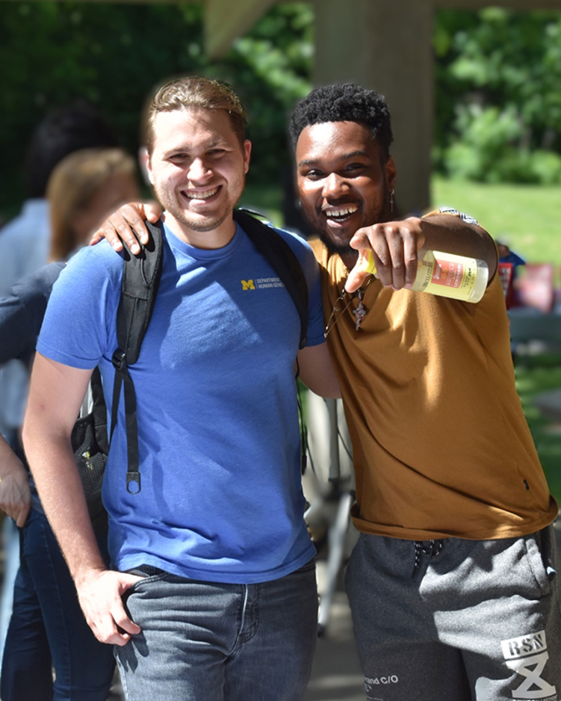 two guys standing together and one laughs and points at camera