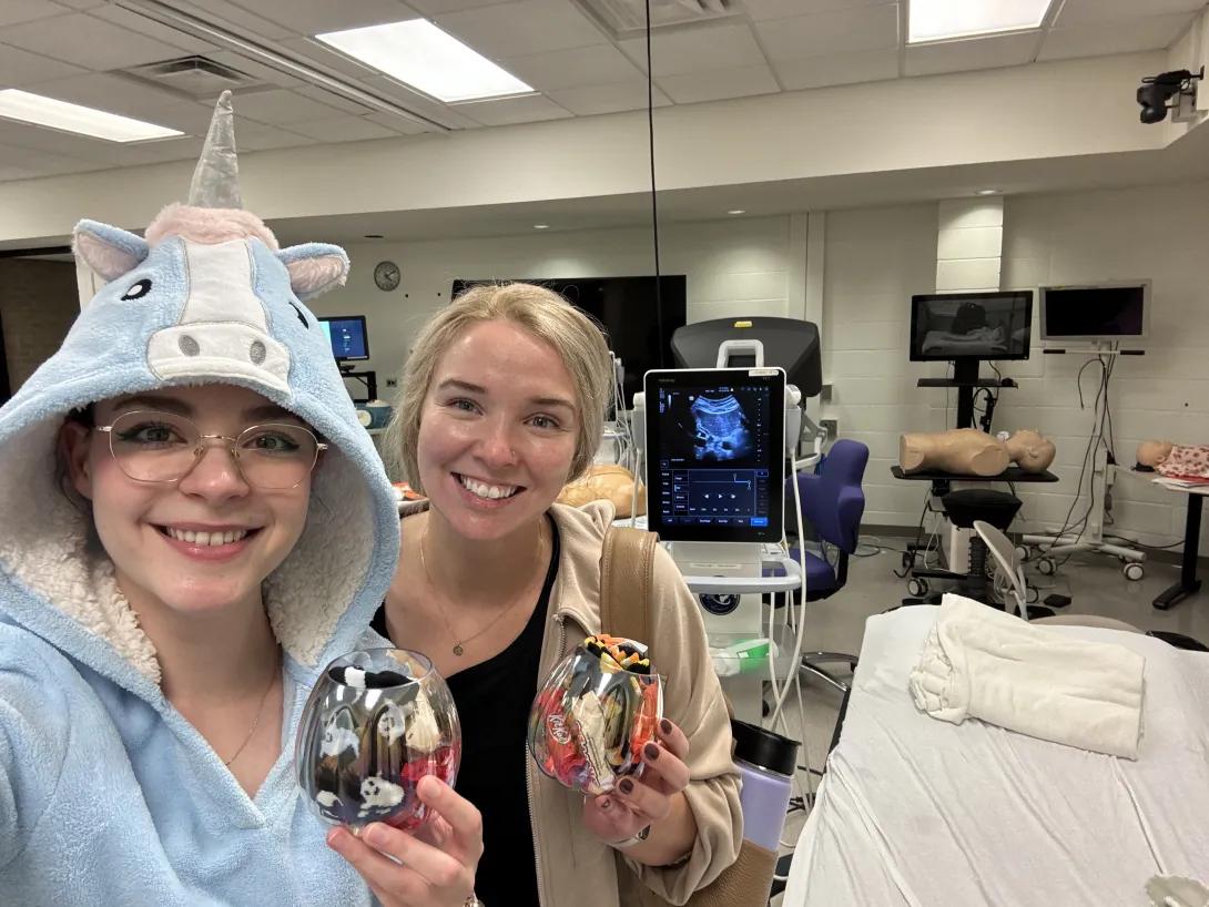 Melis Ozkan wears a unicorn costume and stands next to classmate Laura and an ultrasound simulator