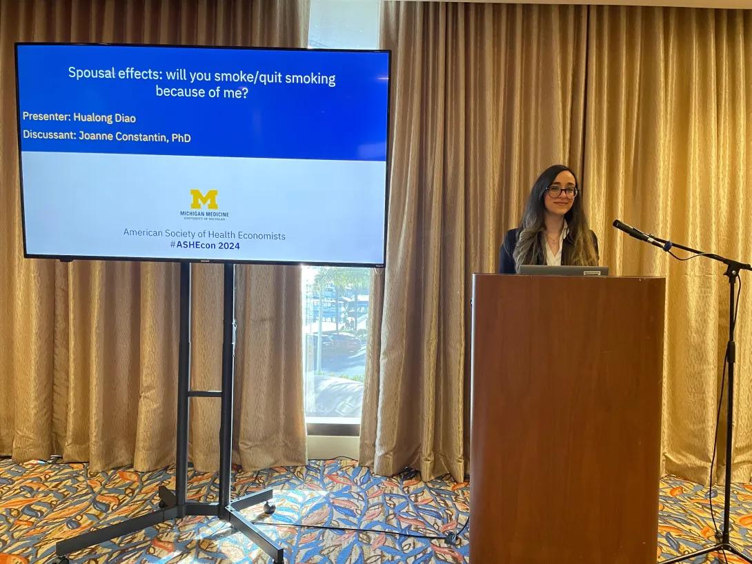 Joanne standing at a podium in front of a power point presentation
