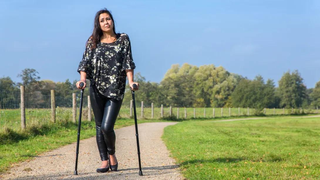 A young woman with disability walks a path with loftstrand crutches
