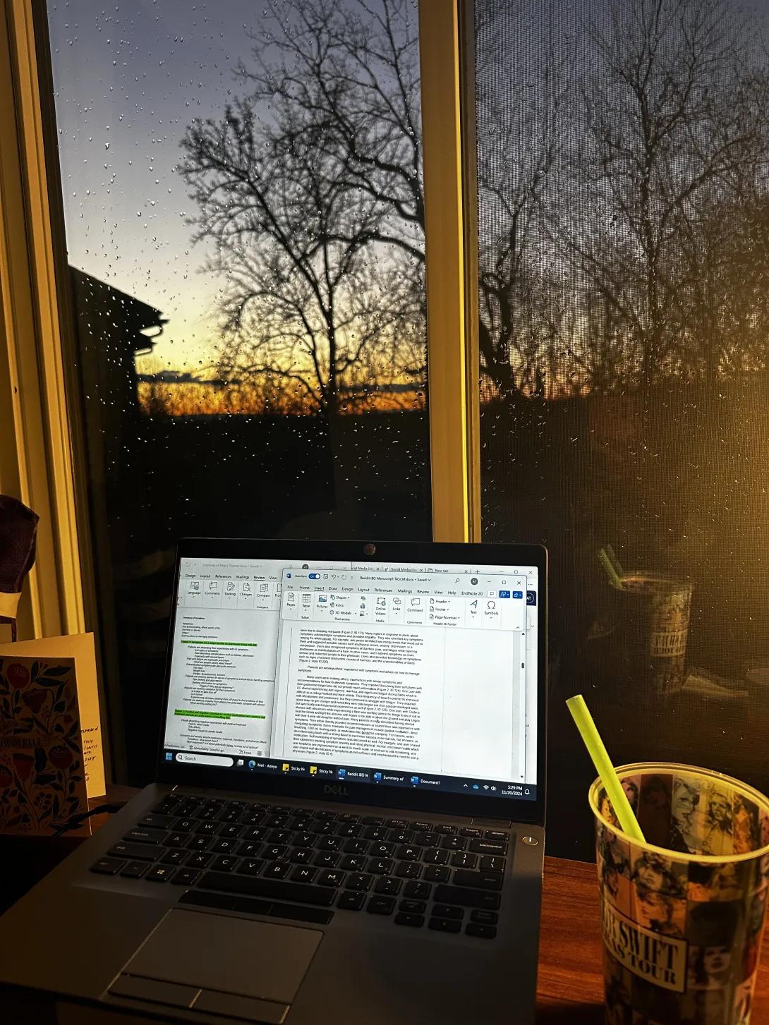Image of an open laptop computer on a desk in front of a window with a sunset in the background